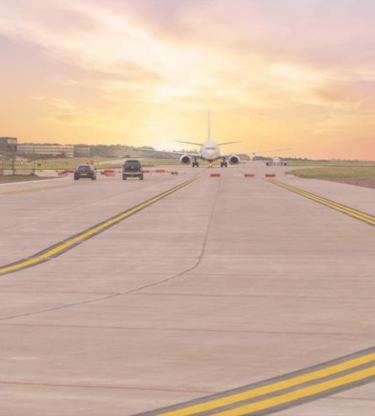 Looking down a runway, with a plan in the distance at sunset