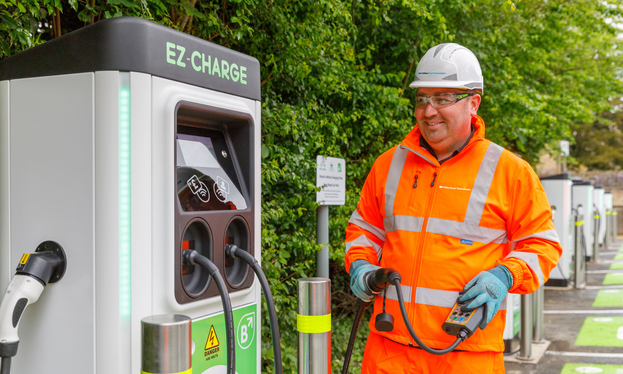 Man in orange PPE holding the cable for a car EV Charger